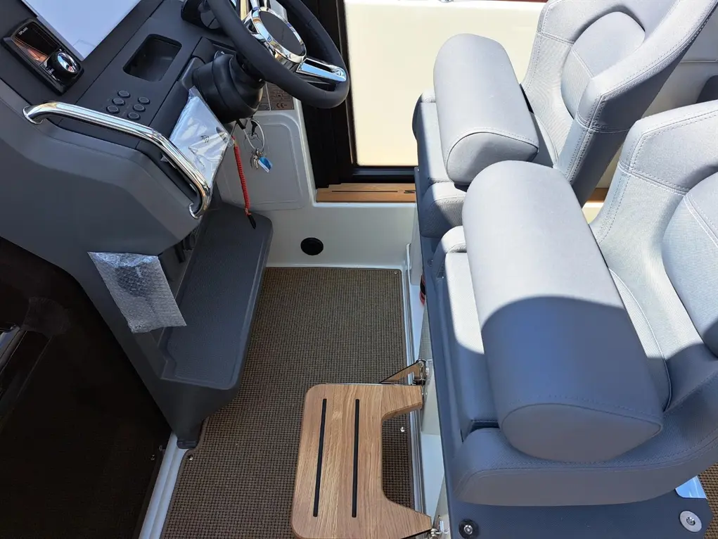 Interior of a boat featuring a steering wheel, grey seats with armrests, and a wooden step. Various controls and keys are visible.
